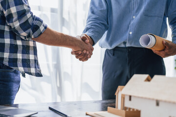 Engineers consulting team close up to design building blueprints paper for clients with building models to work at office. Shaking hands