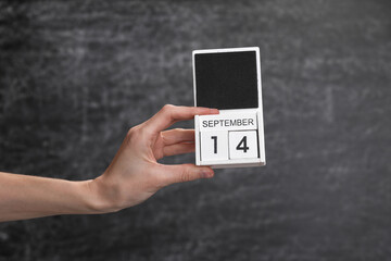 Wooden block calendar with date september 14 in female hand on background of school chalk blackboard
