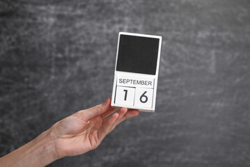 Wooden block calendar with date september 16 in female hand on background of school chalk blackboard