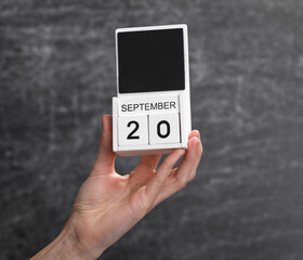 Wooden block calendar with date september 20 in female hand on background of school chalk blackboard