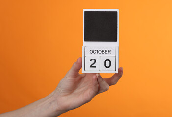 Wooden block calendar with date october 20 in female hand on orange background
