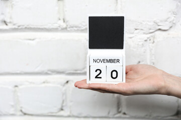 Woman's hand holds wooden block calendar with date november 20 on brick wall background