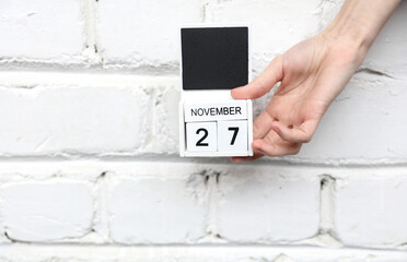 Woman's hand holds wooden block calendar with date november 27 on brick wall background