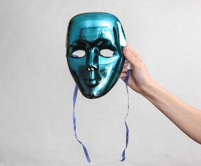 Female hand holding anonymous mask on gray background