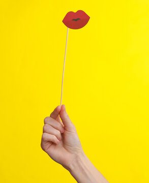 Woman's hand holds lips on stick on a yellow background. Carnival, photo booth, party concept
