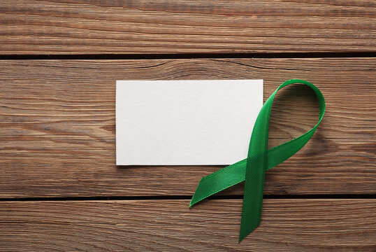 Green awareness ribbon with white banner on wooden table