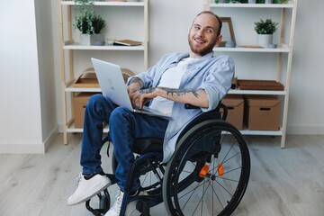 Man in wheelchair freelancer working at laptop at home smile, work online, movement restriction, copy space, integration into society, health concept man with disabilities, real person