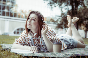 Young woman student doing homework lying in the park on a blanket