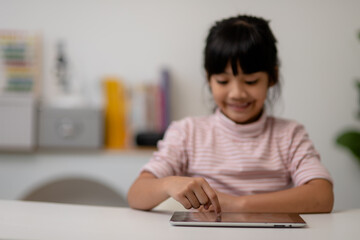 Asian little cute girl touching the digital tablet screen on the table