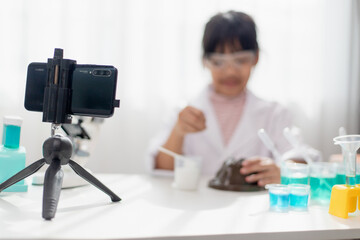 Asian school girl making easy chemistry experiments and recording a video for his followers, Young blogger kid posing in front of camera for vlog, Children make vlog for social media channel concept.