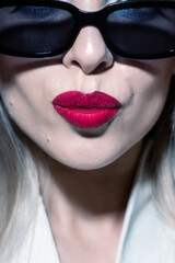 Fashion, make-up and lifestyle concept. Beautiful woman close-up studio portrait with sunglasses and red lipstick making kiss facial expression. Model wearing bright suit. Toned image with blue color