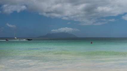 Serene seascape. A boat is racing in the turquoise ocean, a foam trail behind the stern. The silhouette of the island on the horizon. Clouds in the blue sky. The waves roll towards the shore.