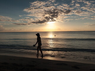 Fototapeta na wymiar Amanecer en una playa del caribe con mar tranquilo, sol saliendo y gente empezando a caminar.