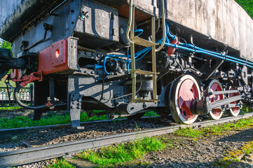 An old rusting steam locomotive is standing on a siding. Wheels and drive of an old steel locomotive. An old black steam locomotive is standing on the rails.