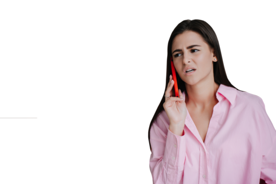 Frustrated young brunette talking by phone with upset expression dressed in pink shirt against ftransparent background. Young woman received bad news, painful expression on face. I can’t hear you