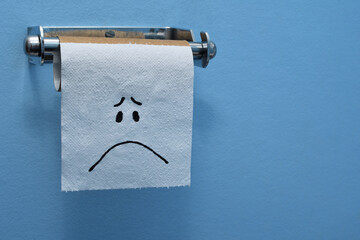 Close-up, sad face on the last piece of toilet paper, tissue on a brown cardboard toilet roll, blue...