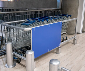 Row of shopping cart with blue handle lined up on wood floor by barrier wall at parking lot