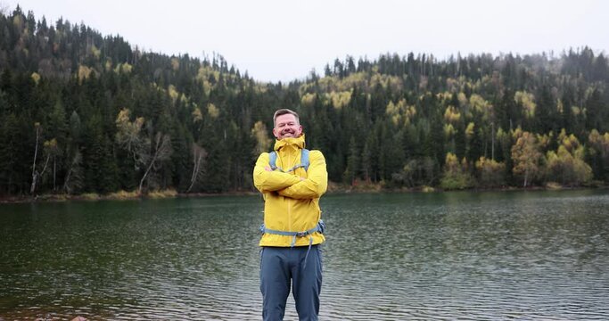 Happy male tourist in rain in forest in mountain lake
