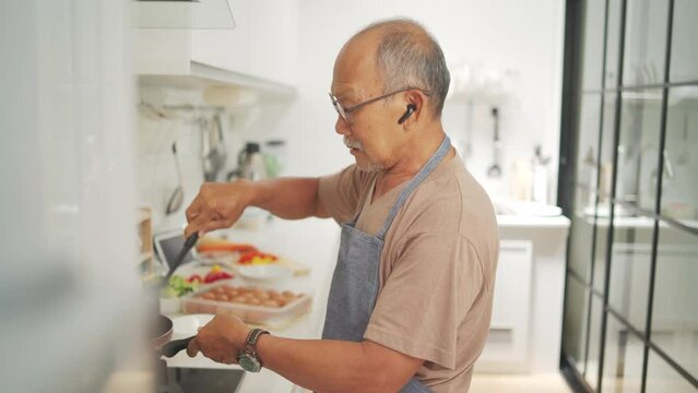 Happy retired Asian Mature Adult male cooking vegetables in frying pan at kitchen, Healthy Food, Prepare Food
