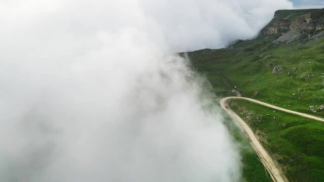 Clouds over green mountains in foggy evening. Aerial drone view, fliying through the clouds. Beautiful summer landscape. Gumbashi Pass in North Caucasus, Russia. 
