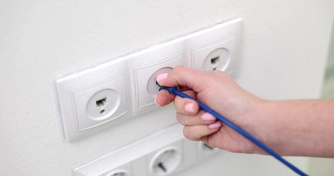 Hand connects internet cable to Wi-Fi extension cord that is in electrical outlet on wall