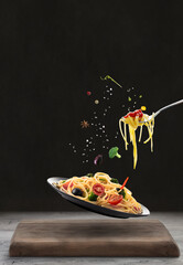 Creative idea-Flying spaghetti with vegetables in a plate- Black background.