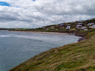 Obraz premium View of Inchydoney beach from the Cape of the Virgin Mary. Irish seascape. A small European settlement on the seashore in summer. Green grass near body of water under cloudy sky
