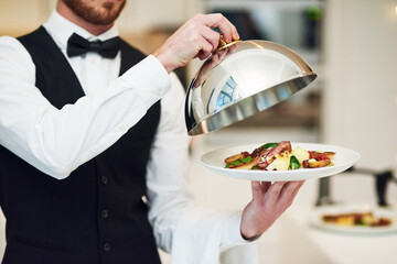 Waiter, hands and opening plate of food for serving, meal or customer service at indoor restaurant. Man employee caterer or server catering or bringing open dish for fine dining, hospitality or order