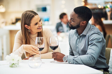 Love, wine and interracial couple on date for fine dining, restaurant or valentines celebration together. Black man and happy woman with romance alcohol glasses, celebrate and luxury in night bokeh
