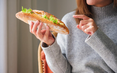 Closeup image of a young woman holding and pointing finger at a piece of french baguette sandwich...