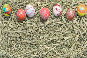 Fototapeta na wymiar Composition de Pâques avec des œufs de poules colorés sur fond avec de la paille. Concept de fêtes de Pâques avec espace vide. Vue de dessus.