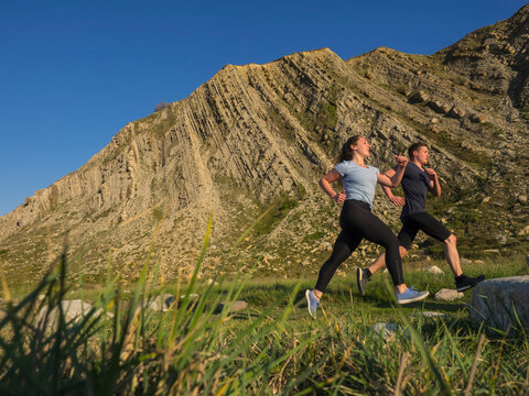 Man and woman running on single trail on cliff of Getxo