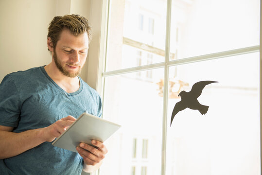 Man using digital tablet standing by window, Munich, Bavaria, Germany