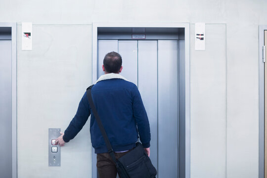 Rear view of a businessman pressing elevator button in an office, Freiburg im Breisgau, Baden-W&uuml;rttemberg, Germany