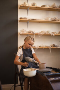 The girl is blow drying a freshly made clay mug on a Potter's wh