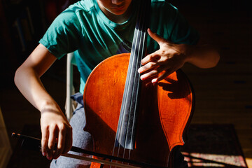Close-up of boy sitting in bright patch of light practicing cello