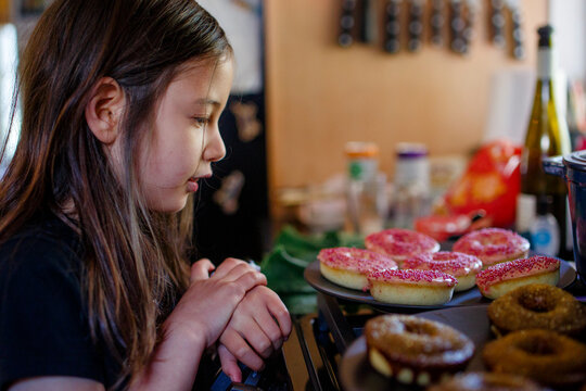 A little girl stares longingly at donuts on countertop