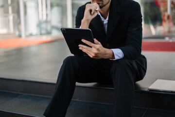  Successful businessman works outdoors near the office holds a tablet