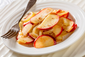 close-up of fried onion and red apple slices on white plate with fork on white wood table