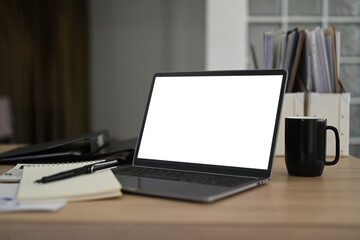 Laptop computer with white empty display, coffee cup and notebooks on wooden office desk