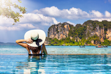 A tourist woman with sunhat in a swimming pool enjoys the view over the popular Railay beach,...