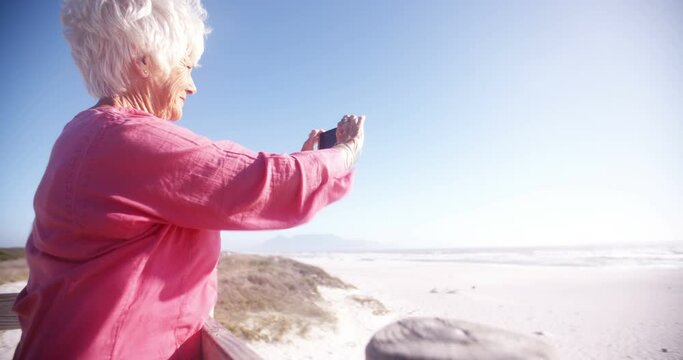 Retired senior woman at the beach taking a picture of the ocean on her phone