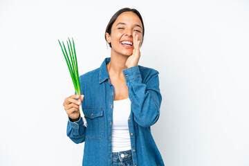 Young hispanic woman holding chive isolated on white background shouting with mouth wide open