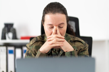 Shot of a female soldier looking stressed out while working in an office