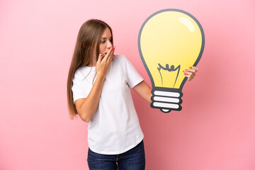 Young Lithuanian woman isolated on pink background holding a bulb icon with surprised expression