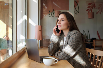 Young beautiful woman having a conversation over the phone in a coffee shop. Remote work concept. Female freelancer working in coffeehouse. Close up, copy space, background