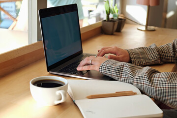 Cropped shot of young woman's hands typing on a laptop in coffee shop. Unrecognizable female freelancer working in coffeehouse. Remote job concept. Close up, copy space, background.