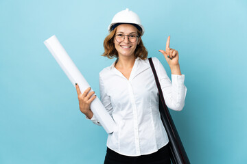 Young architect Georgian woman with helmet and holding blueprints over isolated background pointing up a great idea