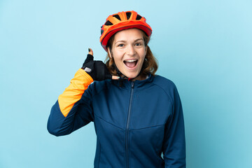 Young cyclist woman isolated on blue background making phone gesture. Call me back sign