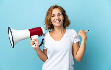 Young Georgian woman isolated on blue background shouting through a megaphone and pointing side